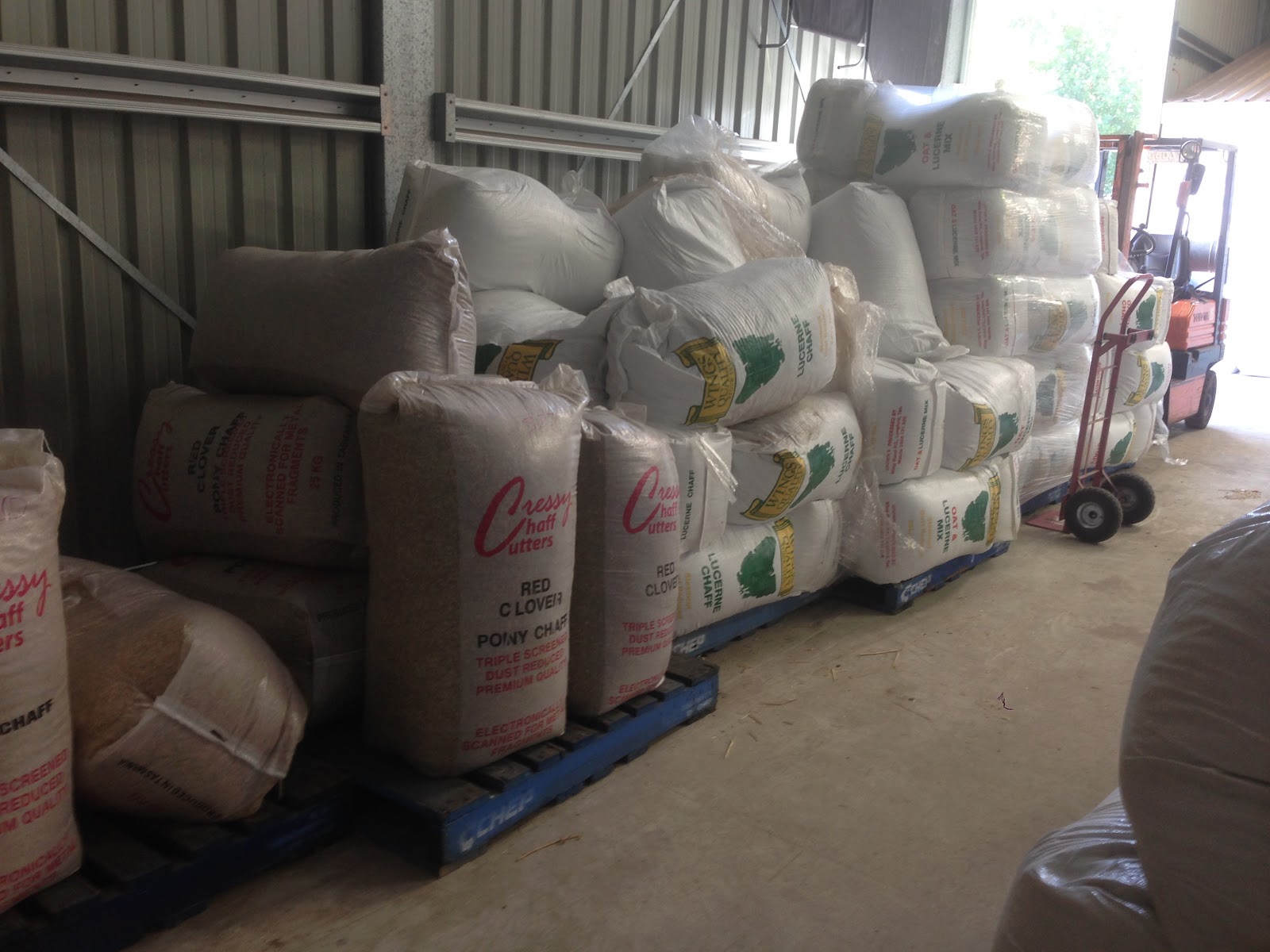 Pallets of bagged feed stacked high inside the shed, with the forklift behind